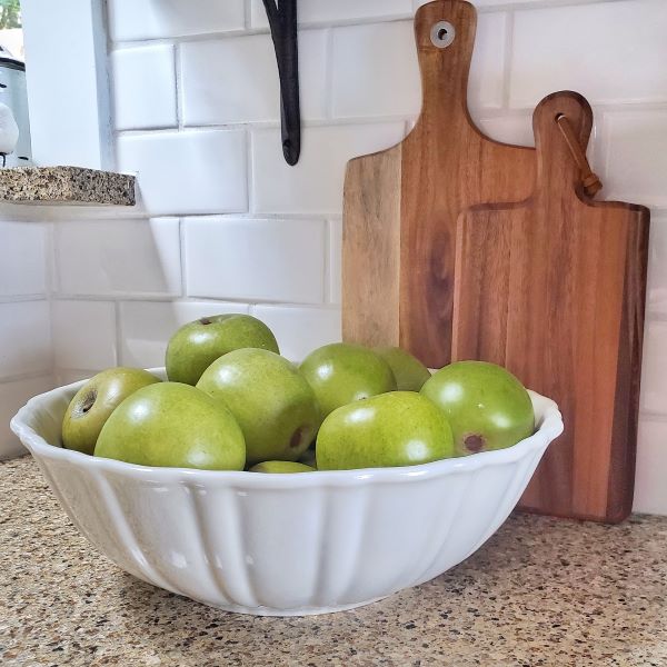 faux green apples in a white bowl on the counter