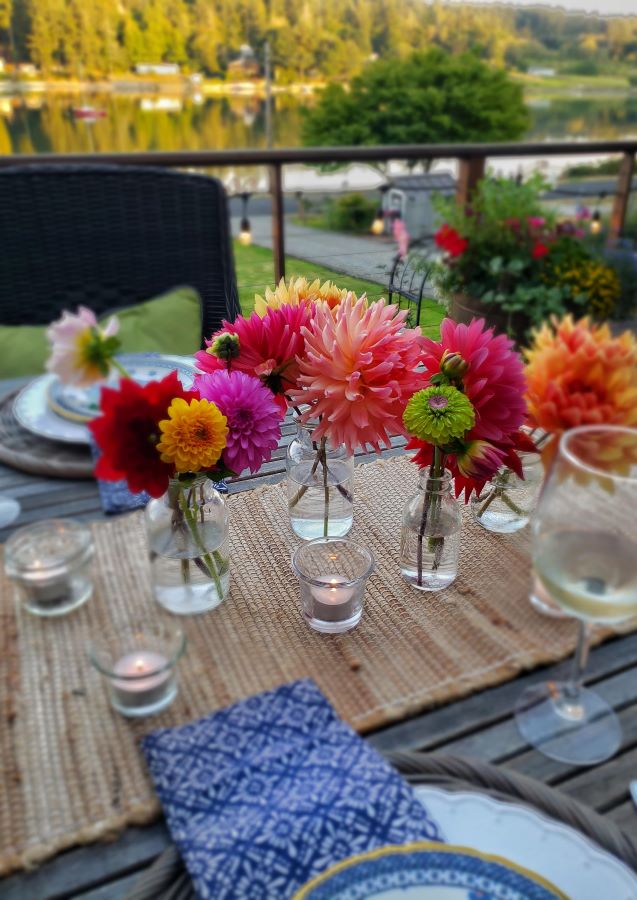Small glass bottles with fresh cut flowers in them and candles on table.