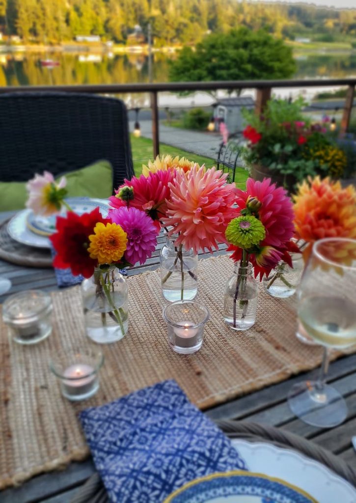 Small glass bottles with fresh cut flowers in them and candles on table.