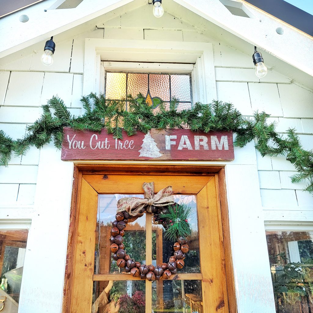 you Cut tree farm rustic wood sign and garland with rustic bell wreath hanging on greenhouse door