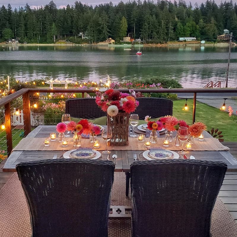 Outdoor dining table with flowers and candles overlooking evening water view