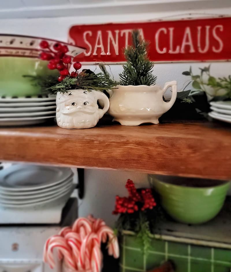 Santa mug with other Christmas decor on open shelves and red Santa Claus sign