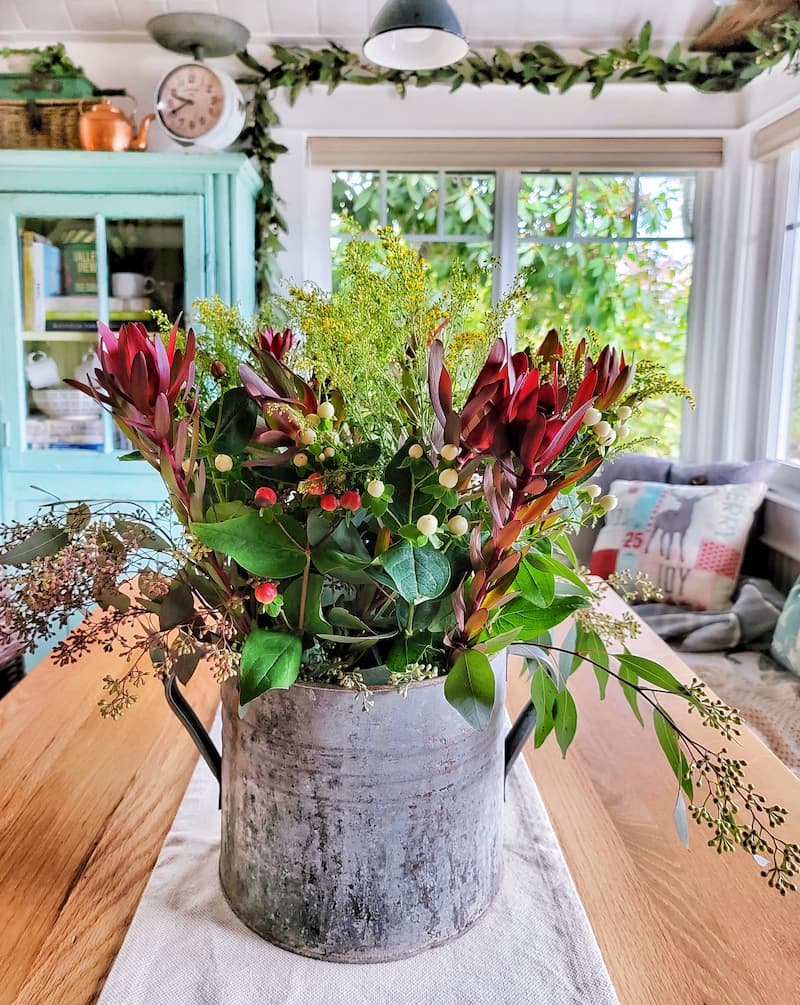 winter seasonal greenery, berries and flowers in vintage galvanized bucket