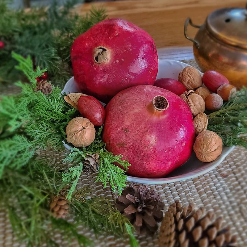 Christmas natural elements:  pomegranates and nuts in bowl with greenery and pinecones
