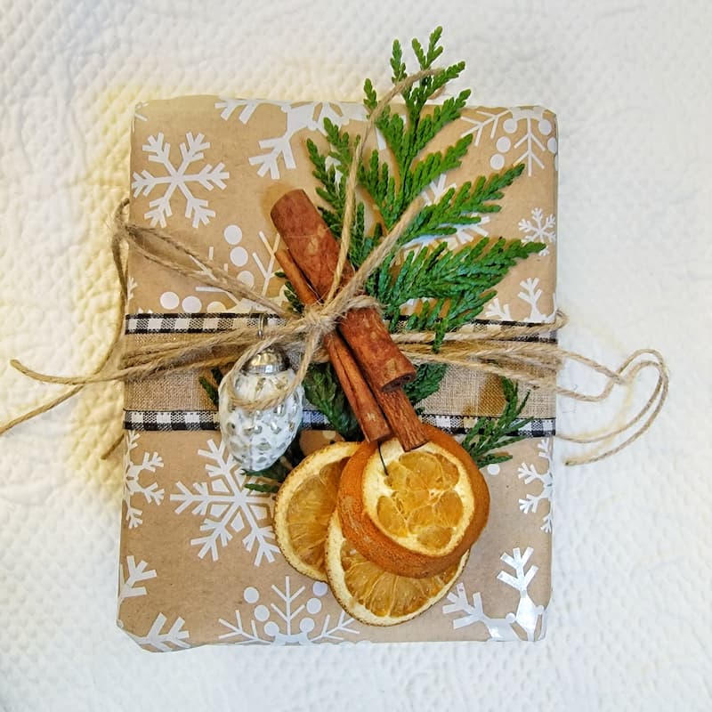 wrapped Christmas gift with cinnamon sticks, dried oranges and greenery