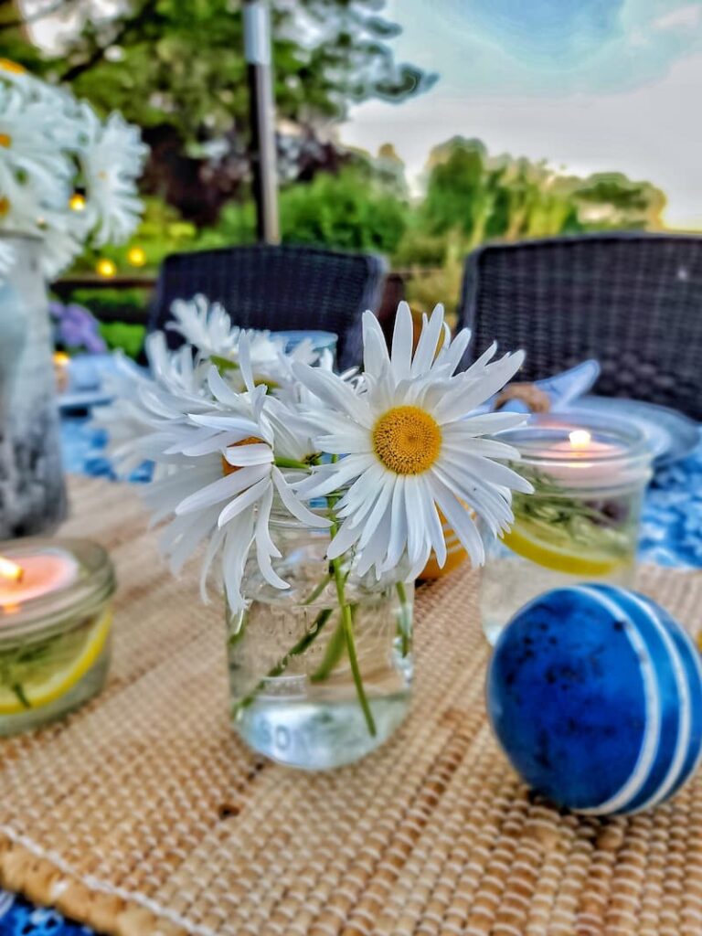 white Shasta daises in a mason jar filled with water and a blue croquet ball on table
