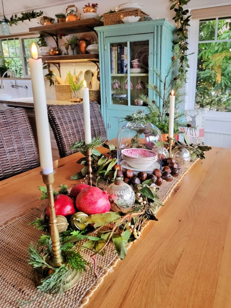  dining room table centerpiece with jute runner, brass candlesticks, pomegranates and glass cloche