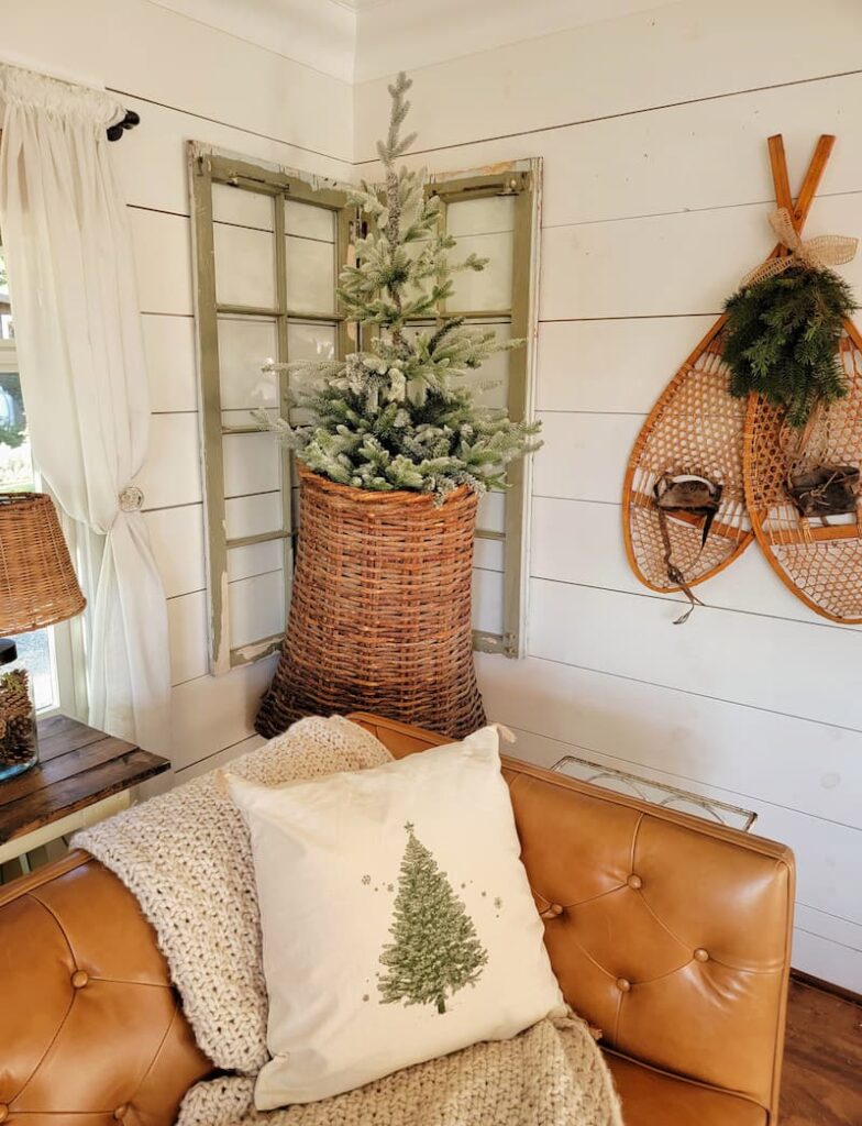 Christmas decor theme: hanging wicker basket with tree in it, snowshoes on the wall and Christmas tree pillow on couch