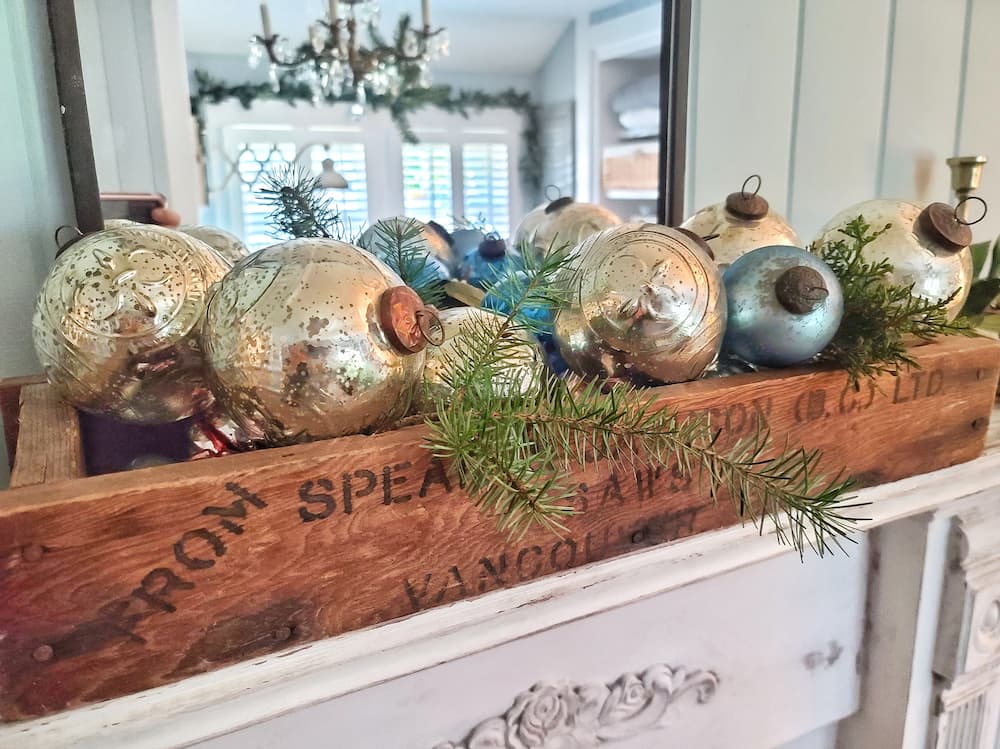 mercury silver and blue ornaments fill a rustic vintage box on the mantel