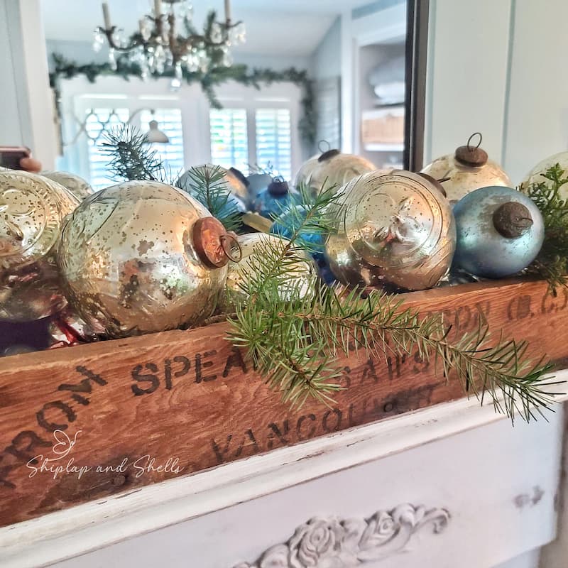 vintage wooden crate and silver and blue Christmas ornaments inside with greenery