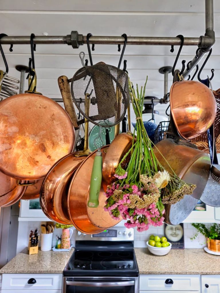 copper pots hanging on rack with dried flowers