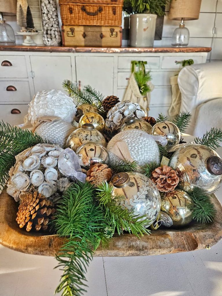 knit and mercury glass Christmas ornaments, with greenery and pine cones in a rustic dough bowl
