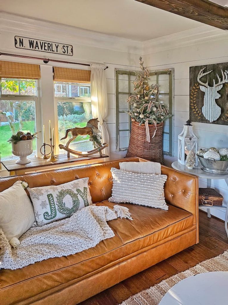 Green and white Christmas decor: leather sofa and pillows next to hanging wicker basket and tree