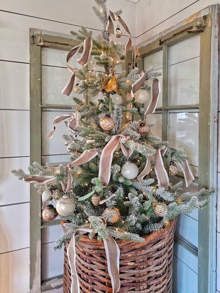 small decorated flocked tree inside vintage hanging wicker basket on green corner windows