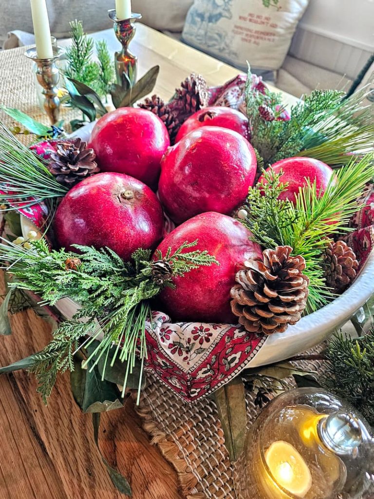 Mixing vintage and modern Christmas decor:  red pomegranates and greenery and pinecones in white bowl