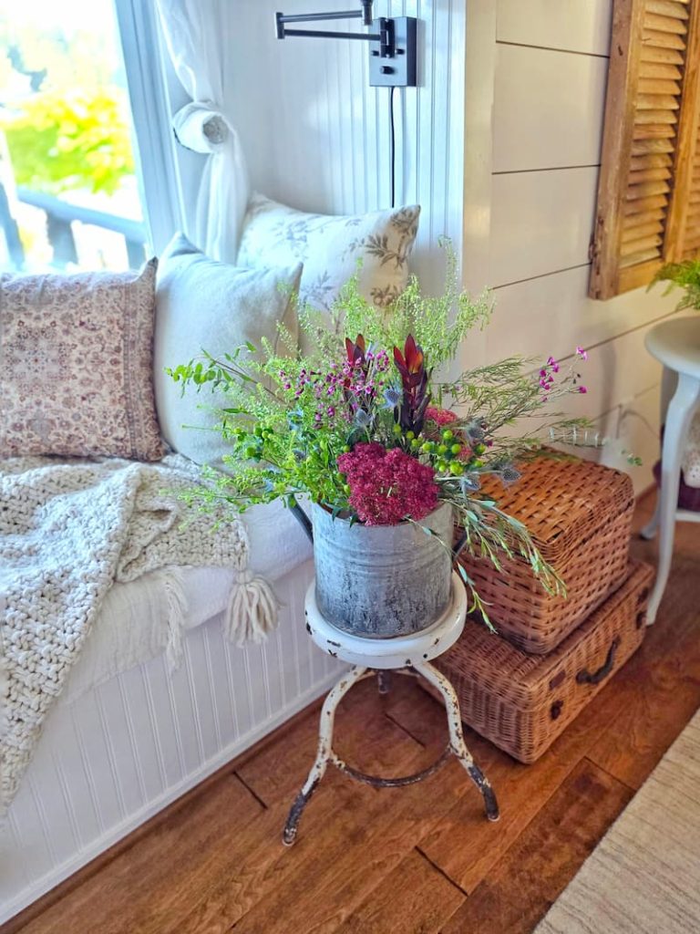 fall pillows on window seat, wicker picnic baskets and vintage galvanized bucket with fall flower arrangement