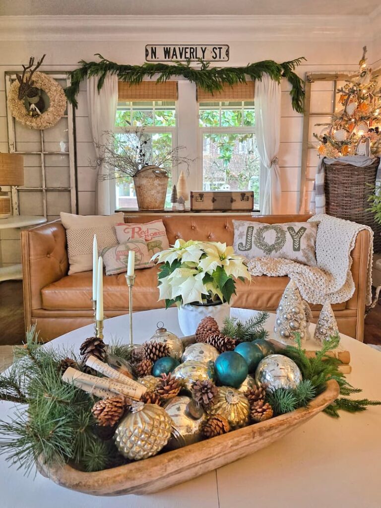 wooden dough bowl with ornaments and pinecones in front of leather couch