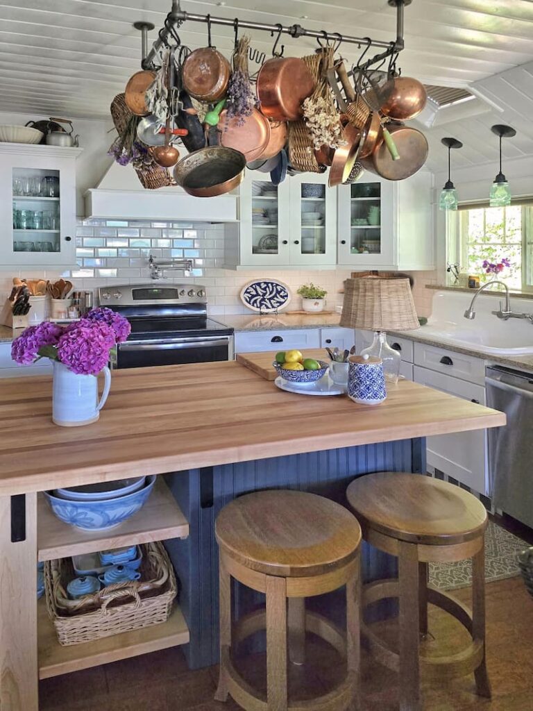 cottage kitchen with butcher block top island with iron pot rack hanging above with copper pots and pans
