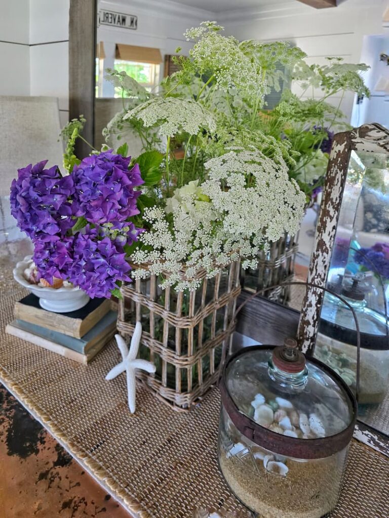 purple hydrangeas and Queen Anne's lace flowers in a wicker and glass vase indoors