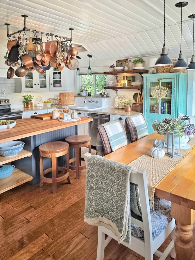 cottage kitchen decorated for fall with copper pans on the pot rack, muted throws, and dried hydrangeas on the table.