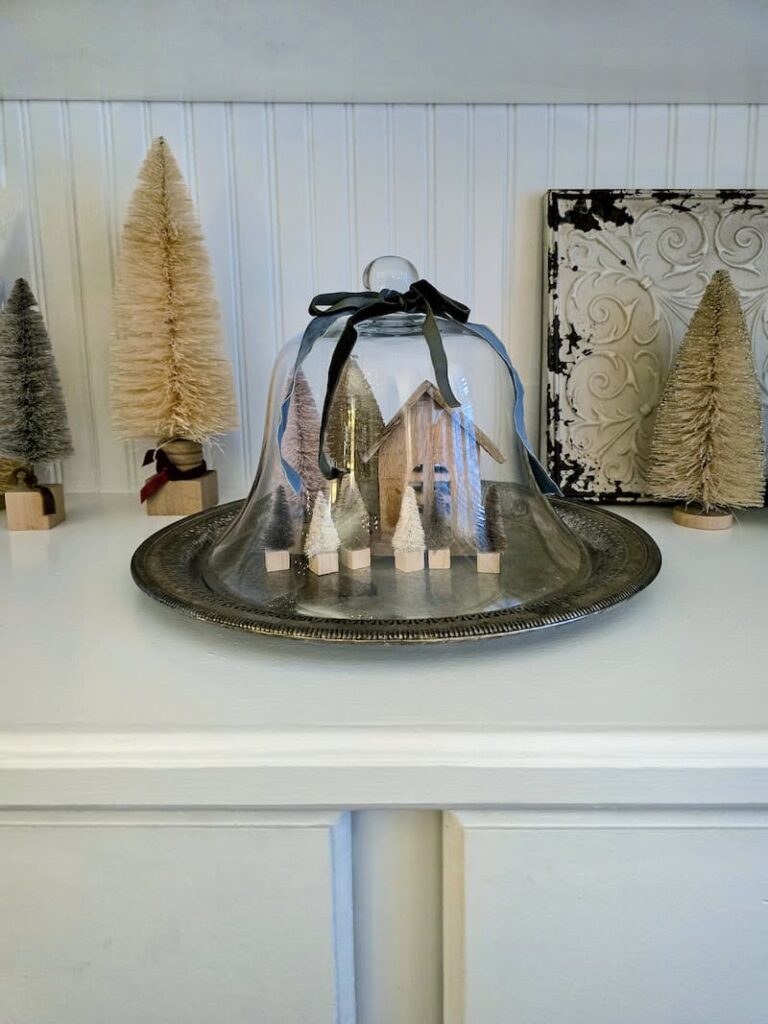 Neutral colored Christmas decor including bottle brush trees and glass cloche with vintage silver tray