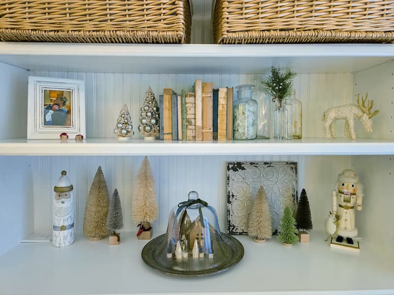 Neutral colored Christmas decor including bottle brush trees and glass cloche with vintage silver tray, nutcracker, and vintage books