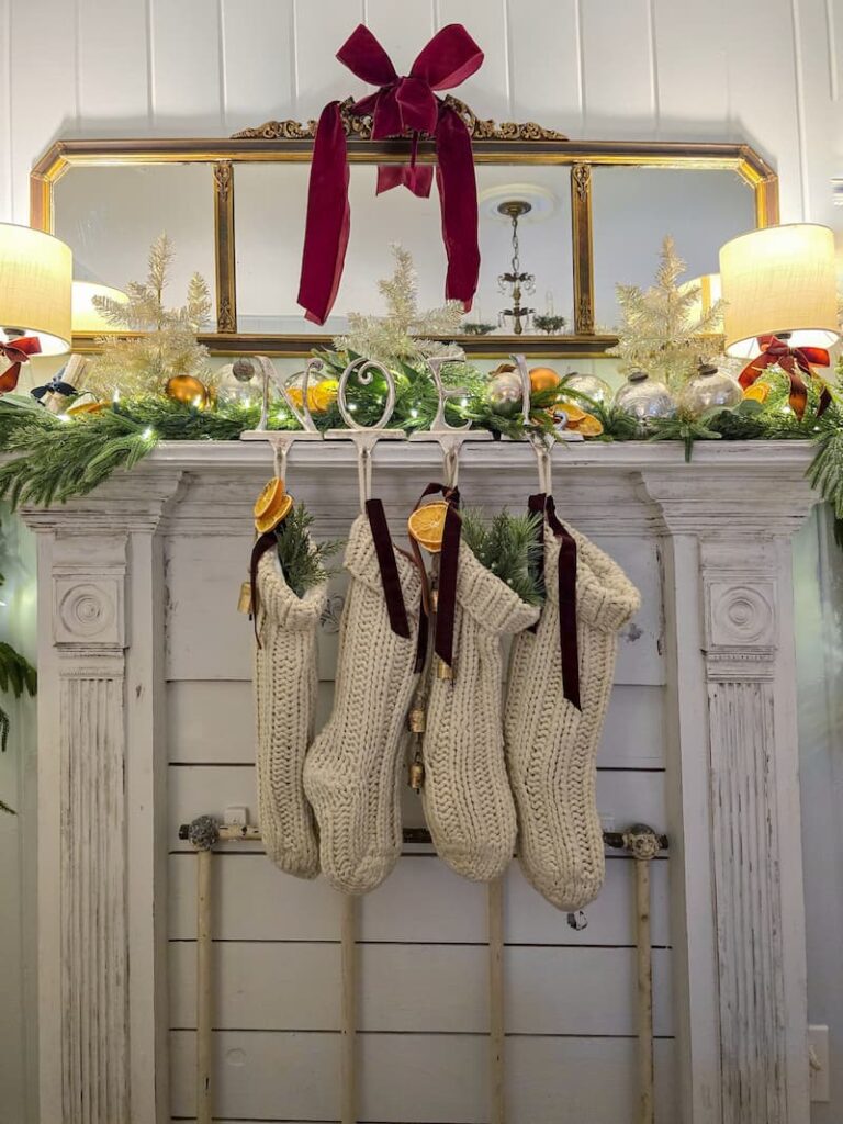 faux fireplace mantel decorated for Christmas with garland, cream knit stockings and a burgundy bow on mirror hanging above