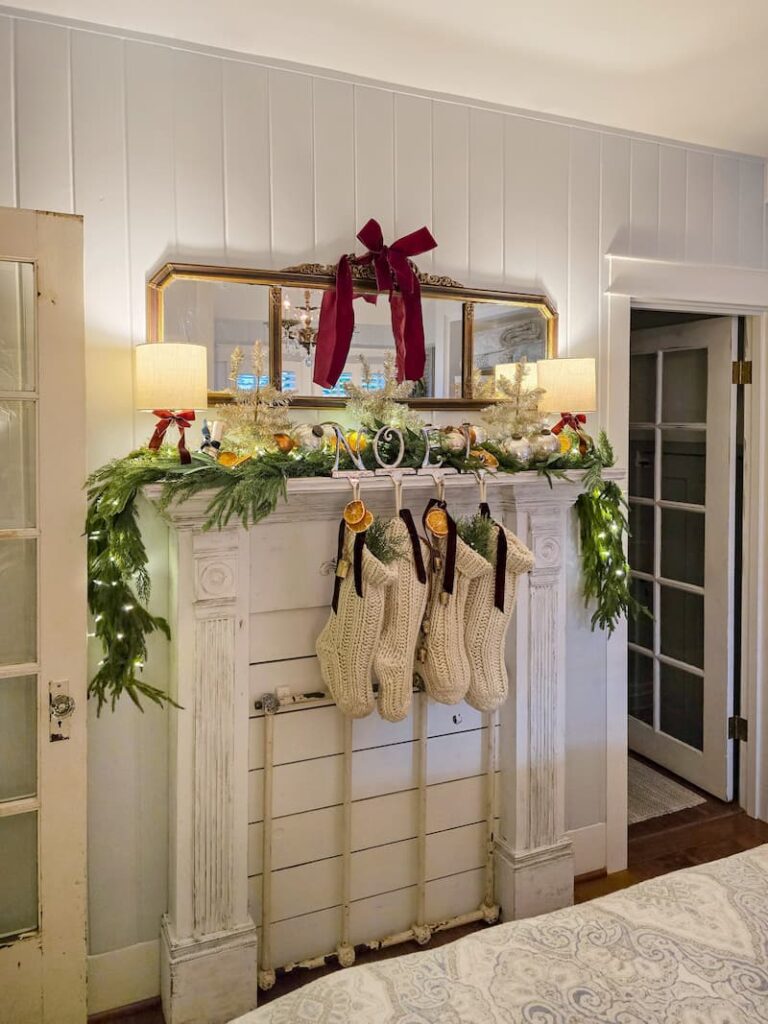 faux fireplace mantel decorated for Christmas with garland, cream knit stockings and a burgundy bow on mirror hanging above