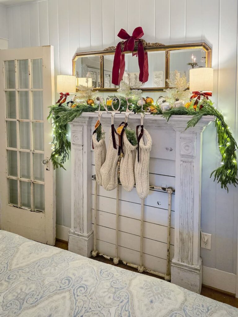 faux fireplace mantel decorated for Christmas with garland, cream knit stockings and a burgundy bow on mirror hanging above