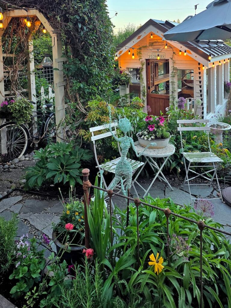 greenhouse and stone patio with a bistro table and chairs, and a teal-colored wire garden fairy