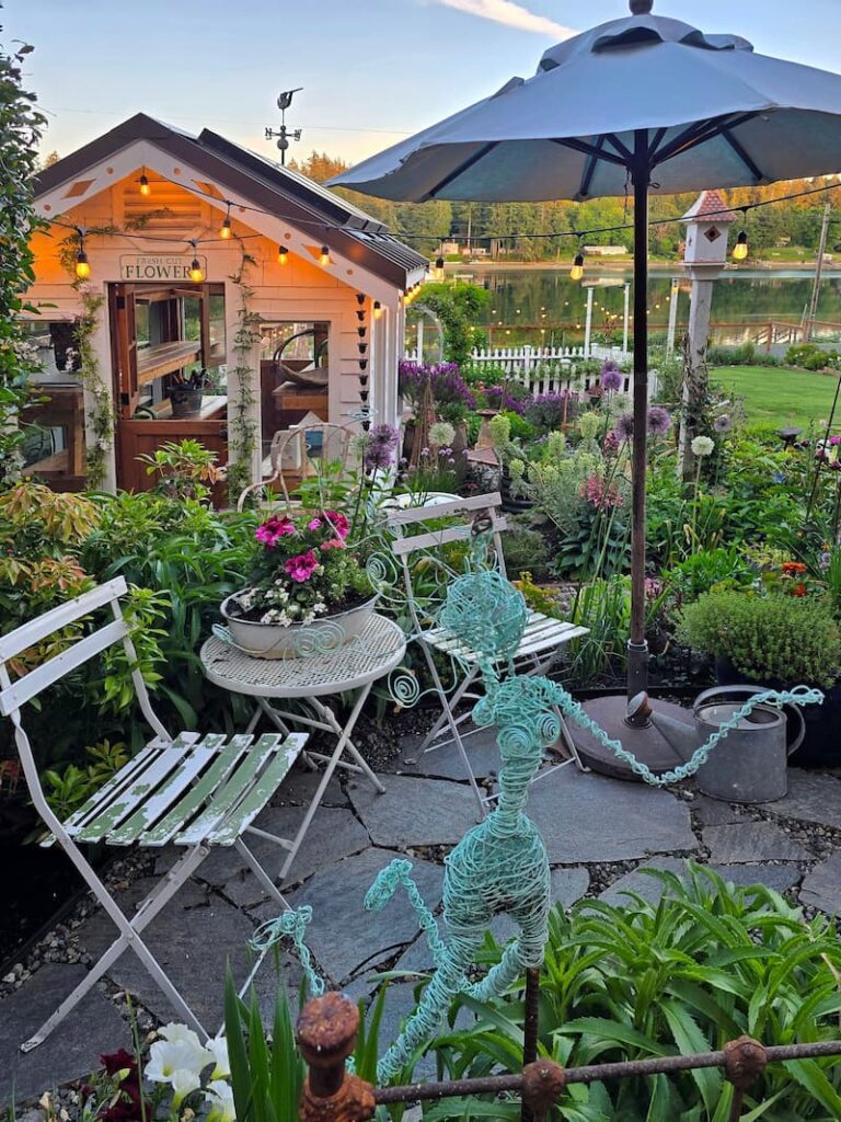 greenhouse and stone patio with a bistro table and chairs, and a teal-colored wire garden fairy