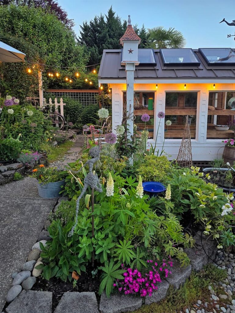 greenhouse and May garden at dusk with lupine, a garden fairy and alliums
