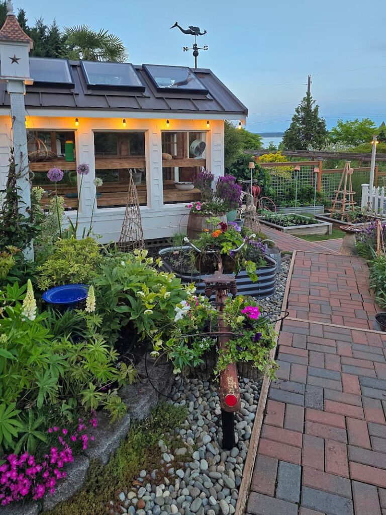 greenhouse and May garden at dusk with a birdhouse and pathway