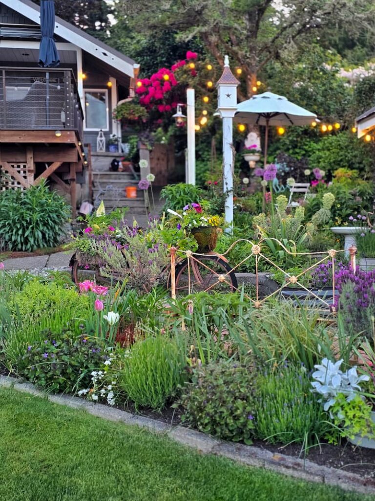 cottage garden in May with a birdhouse, and a vintage headboard in the garden