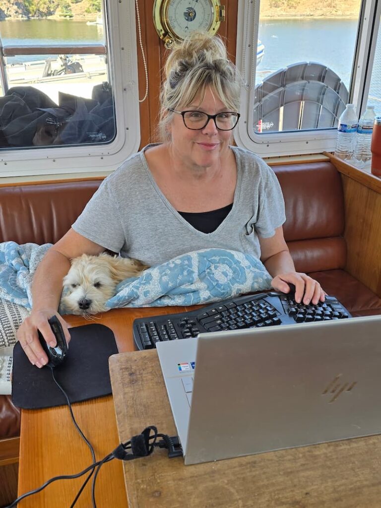 working on the laptop with a cream dog on my lap in the pilot house