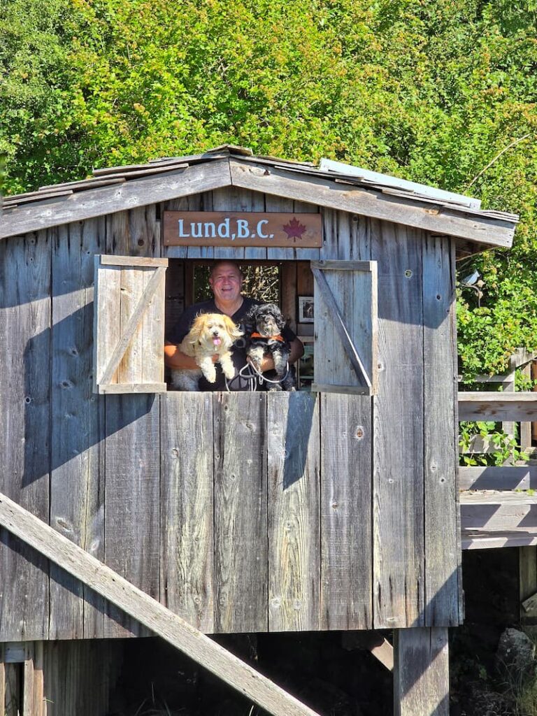 wooden shed with window open showing a man and two dogs in Lund BC