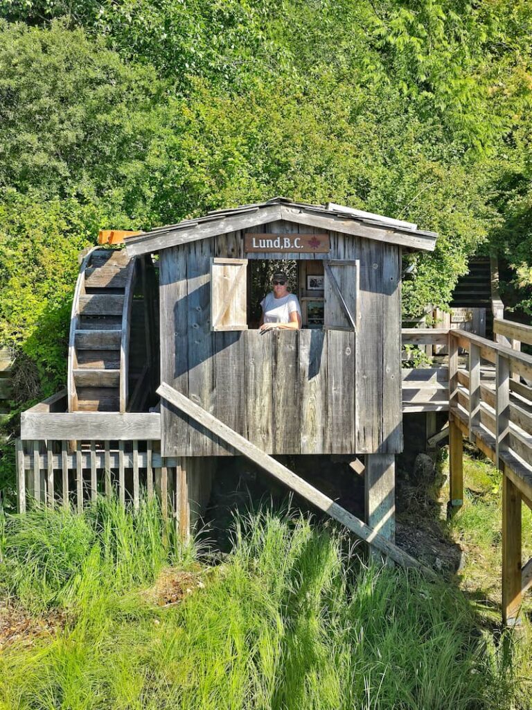 waterwheel attached to a wooden shed with window open showing a woman