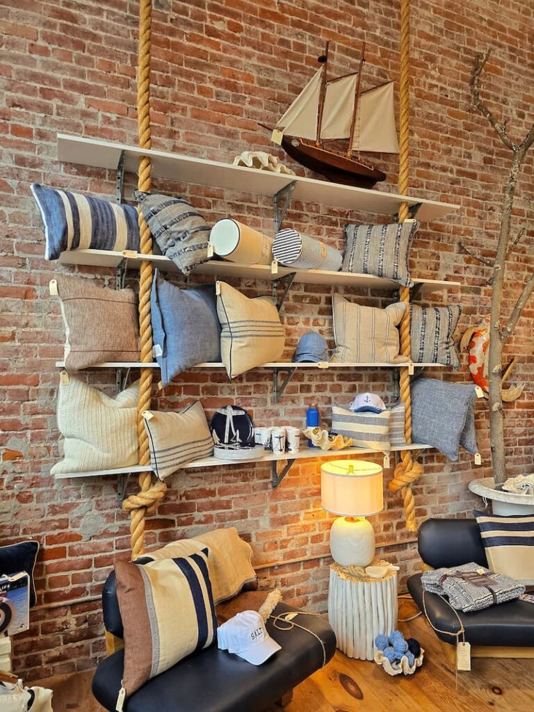 decorative coastal-inspired pillows on shelves against a brick wall inside the Conservatory store