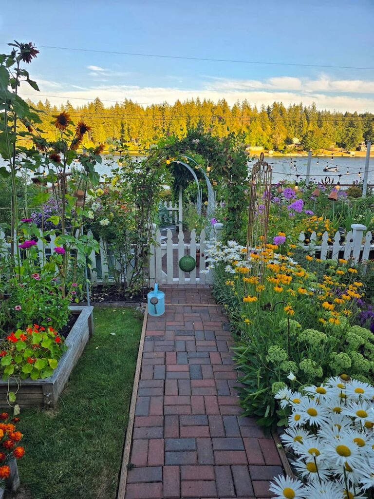 Cottage garden pathway leading through an arbor to a white picket fence