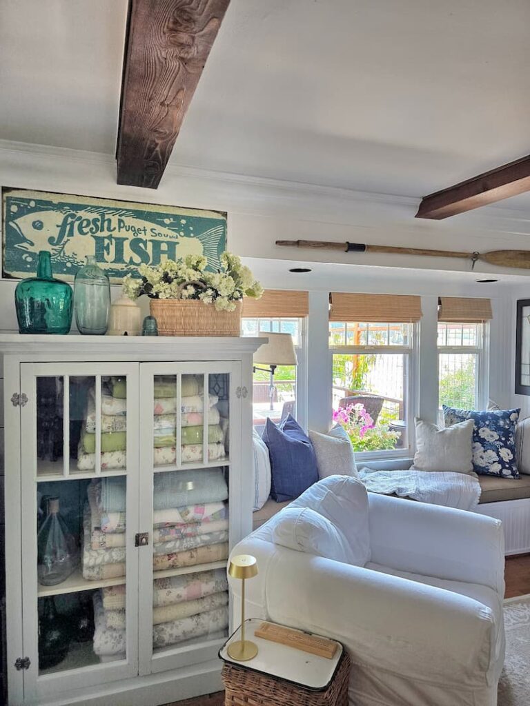 Bright and airy cottage living room in late summer with fresh fish teal and cream metal sign and glass door cabinet