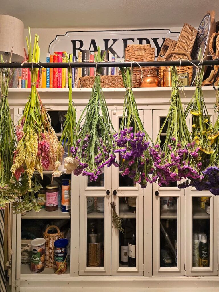 Bundles of dried yarrow, statice, celosia, and strawflower hanging in a cottage pantry