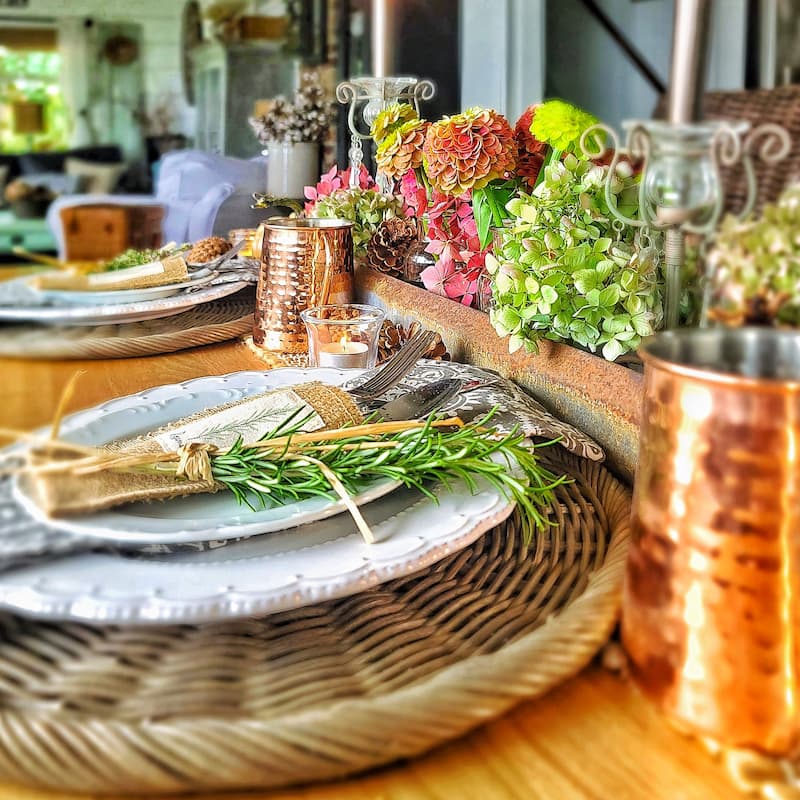 fall tablescape with fresh herbs on white plates and flowers in chicken feeder
