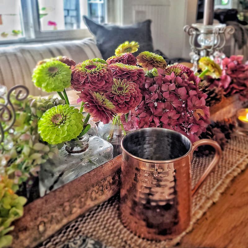 green and rose zinnias and hydrangeas centerpiece and copper mug on table