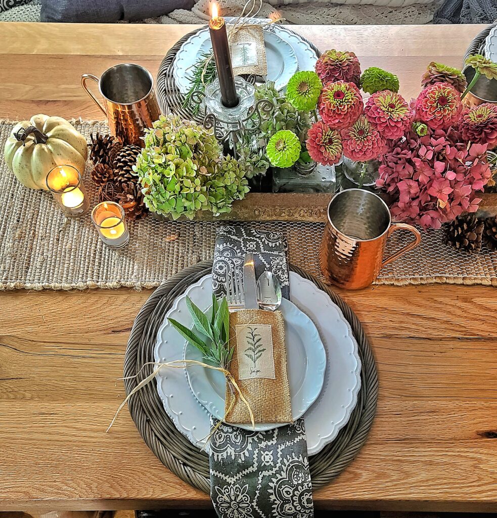 Fall tablescape with sage and herb packet on white dishes and gray and white patterned napkin, hydrangeas, and zinnias

