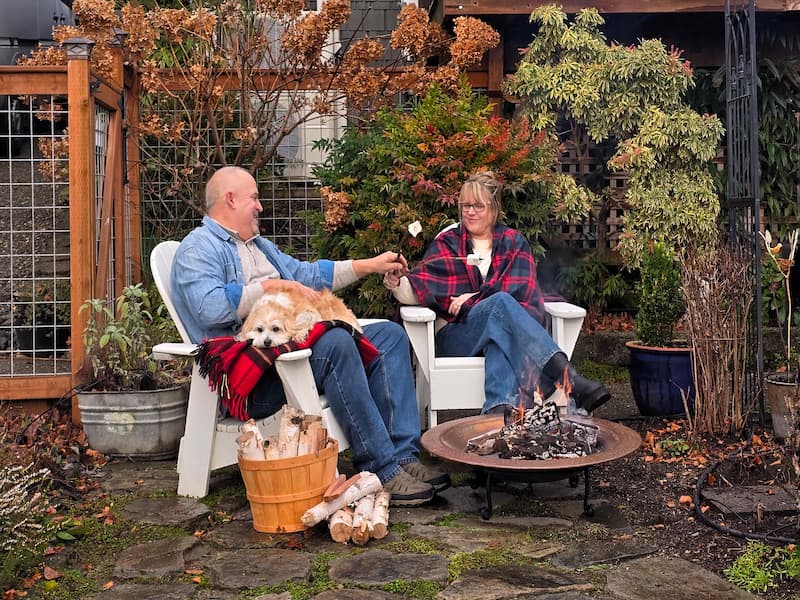 Couple in plaid roasting marshmallows by the fire pit with their dog