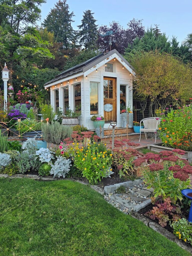 Greenhouse and birdhouse framed by fall perennials