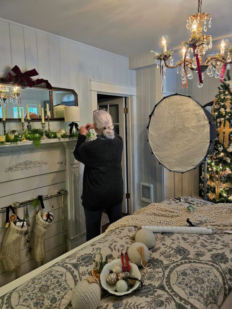 Magazine stylist arranging Christmas greenery on a bedroom mantel